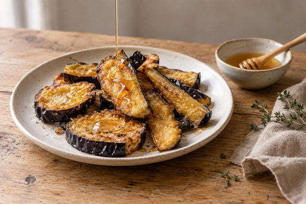 Berenjenas fritas doradas en un plato, con un hilo de miel por encima