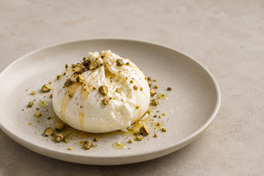 Burrata con miel y pistachos tostados sobre un plato claro
