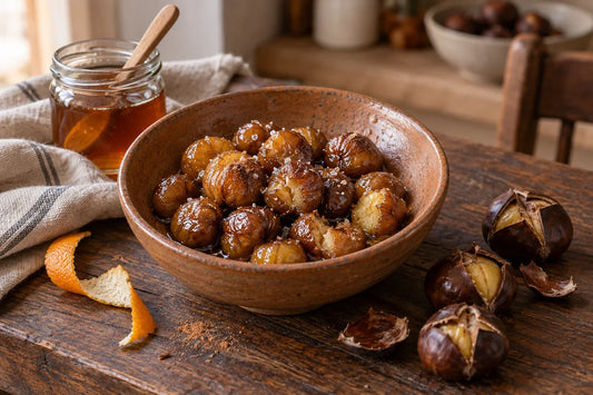 Cuenco de castañas peladas y glaseadas con miel, junto a castañas asadas con la cáscara abierta y un tarro de miel.