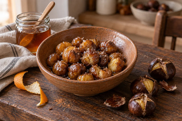 Cuenco de castañas peladas y glaseadas con miel, junto a castañas asadas con la cáscara abierta y un tarro de miel.
