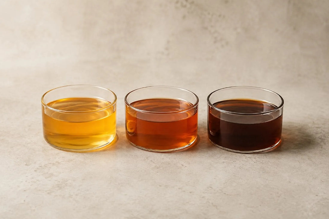 Tres muestras de miel clara, ámbar y oscura en recipientes de vidrio idénticos para comparar su color.