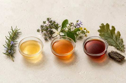 Tres muestras de miel clara, ámbar y oscura junto a flores variadas y una hoja de roble