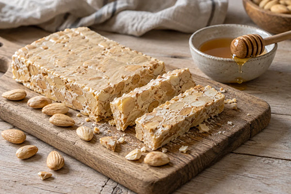 Tableta de turrón duro de almendra cortada en porciones, con miel y almendras alrededor.